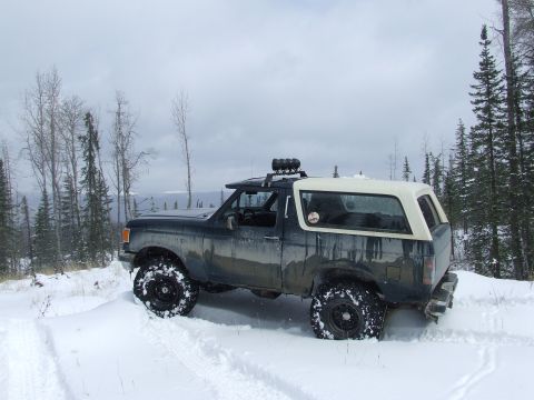 1988 Ford Bronco - A 1988 Ford Bronco navigates a snowy trail, its off-road tires kicking up snow.