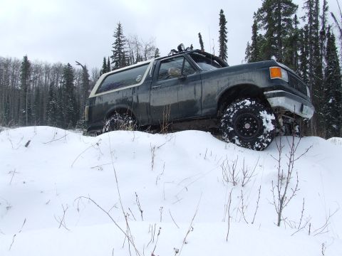 1988 Ford Bronco - Ford Bronco navigates a snowy terrain with tall trees visible behind it.