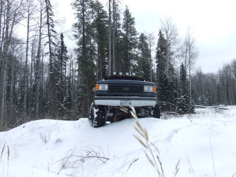 1988 Ford Bronco - A lifted Ford Bronco navigates a snow-covered terrain surrounded by a dense forest.