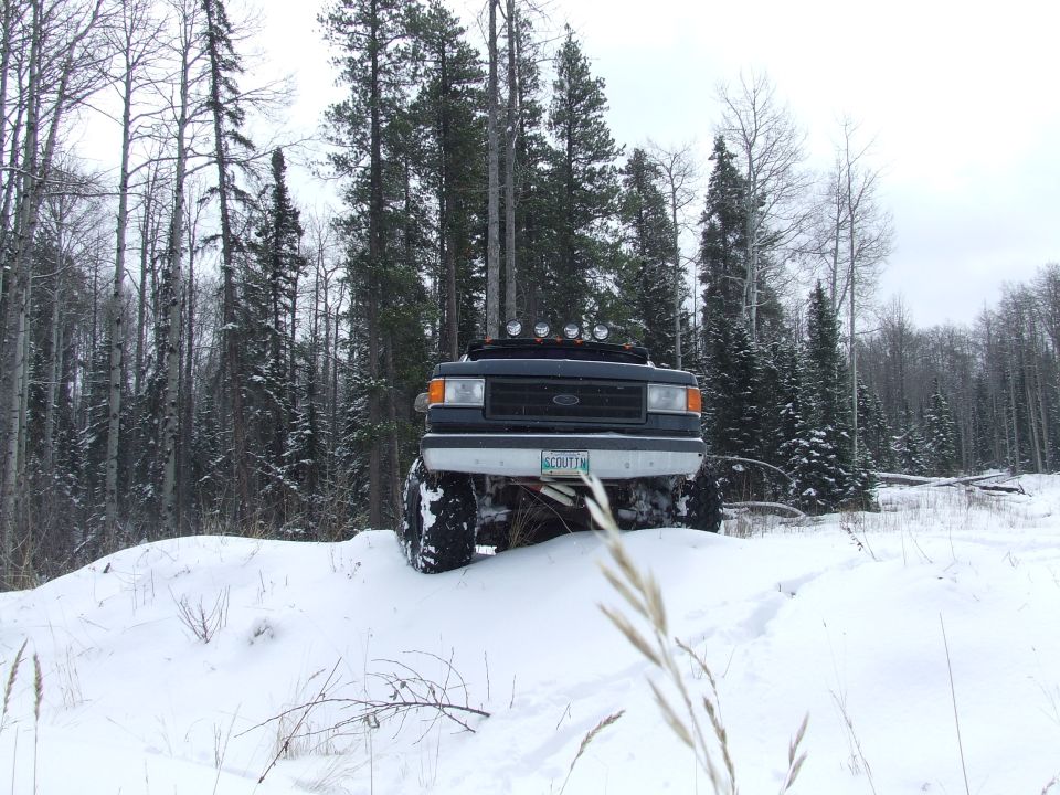 Dark Ford Bronco with off-road tires on a snowy hill, trees in background