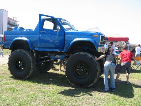 1979 Ford Bronco - A heavily modified blue Ford Bronco sits on a grassy field with its driver's door open.