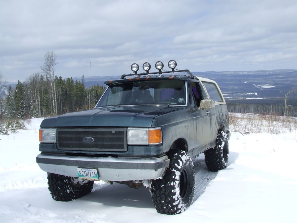 Dark green SUV with off-road tires and roof lights parked in snow