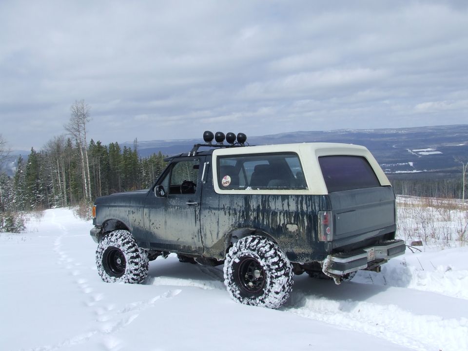 Lifted dark green Ford Bronco with cream top parked in snow above a valley