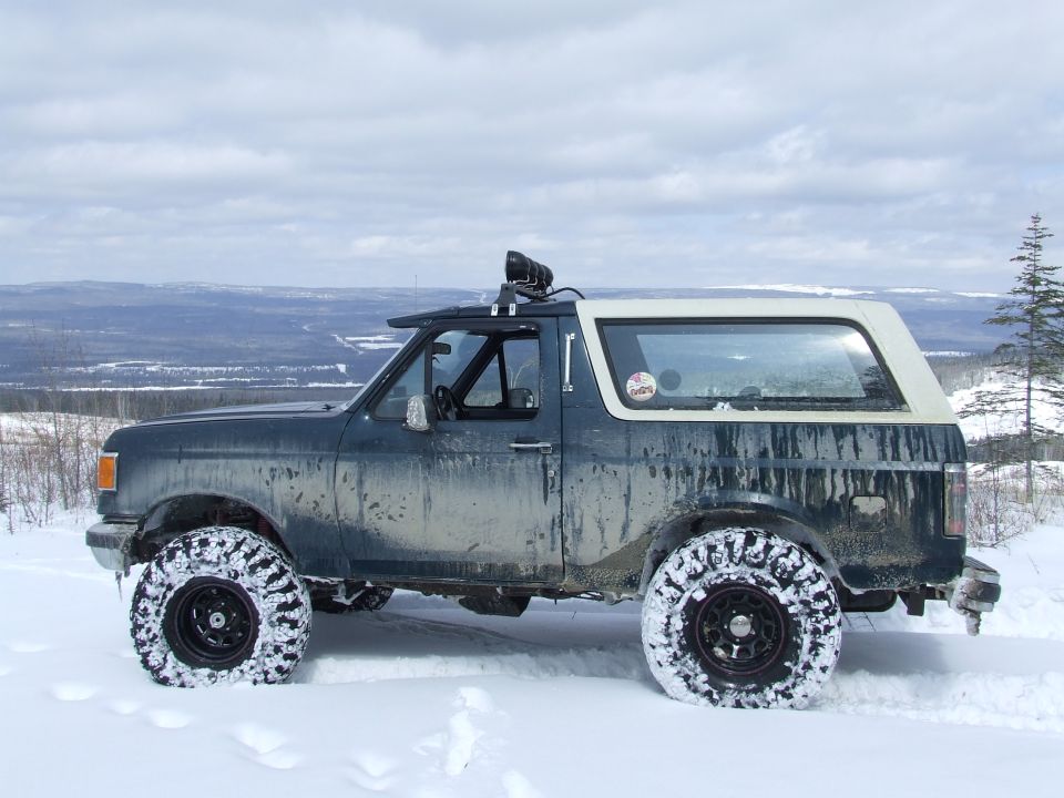 Lifted dark green Ford Bronco with white top parked in deep snow on a ridge