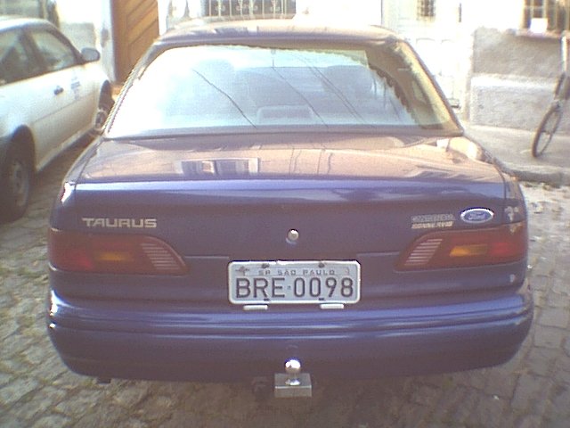 Rear of a purple Ford Taurus with a trailer hitch. Another white car is parked to the left