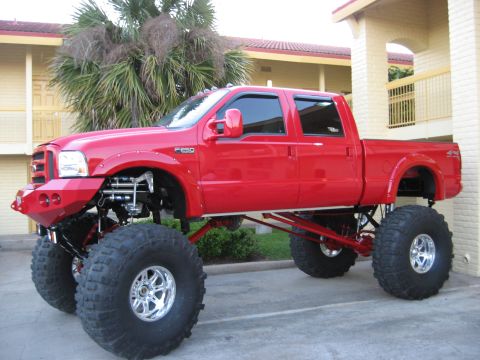 1979 Ford Bronco - This heavily modified red pickup truck features an extreme lift kit and oversized tires, giving it a commanding presence.