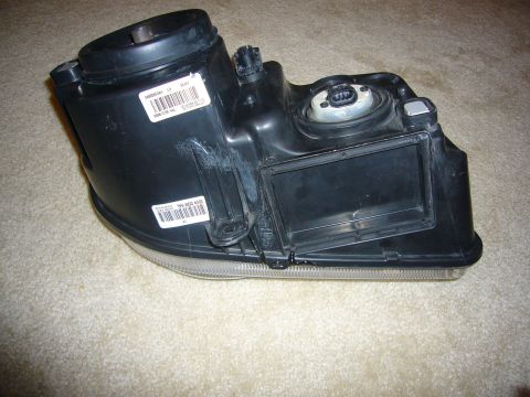 2007 Chrysler 300 - A black headlight assembly is shown, with two white labels containing barcodes and text visible on its casing.