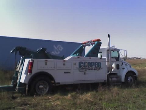 1992 Ford Bronco - A white tow truck with teal accents and 'Cooper Services' branding is parked in a grassy area under a clear blue sky.