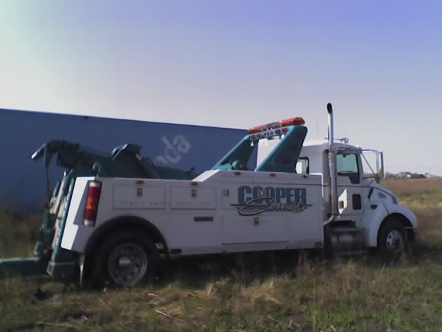 White tow truck with teal accents and 'Cooper Services' logo, parked in grassy field