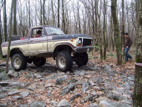1996 Ford Bronco - A lifted Ford Bronco navigates a challenging rocky terrain in a wooded area.