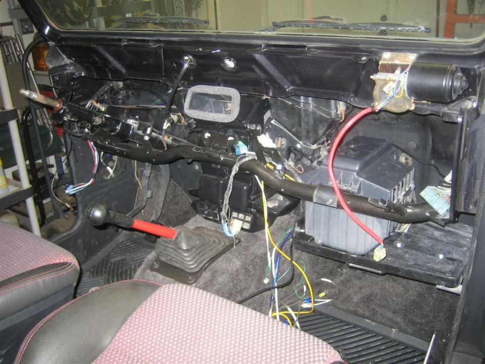 Bare firewall and heater box of a vehicle with dash removed, wiring and red cable exposed