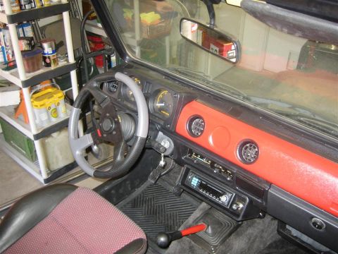 1987 Suzuki Samurai - The interior of a Suzuki Samurai shows a red dashboard, aftermarket steering wheel, and a stereo system.