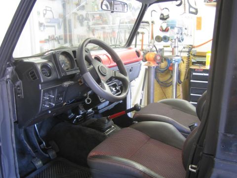 1987 Suzuki Samurai - The interior of a 1987 Suzuki Samurai shows a dashboard, steering wheel, and seats with red accents.