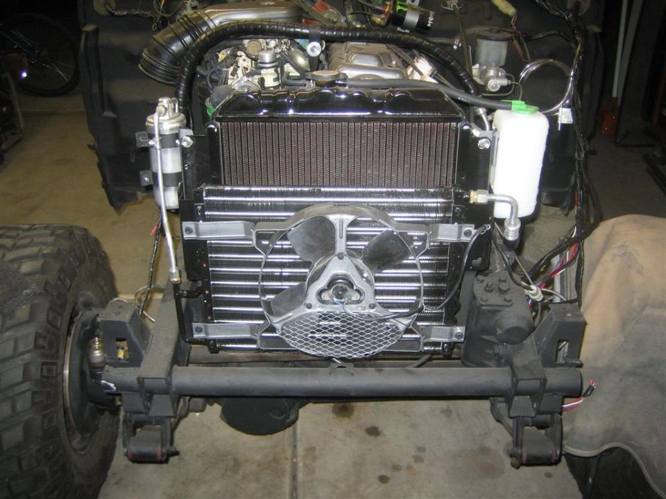 Front view of a vehicle's engine bay, showing the radiator, fan, and some engine components. The vehicle is partially disassembled