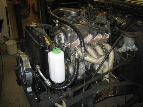 1987 Suzuki Samurai - The engine bay of a 1987 Suzuki Samurai shows the exhaust manifold, radiator, and coolant reservoir.