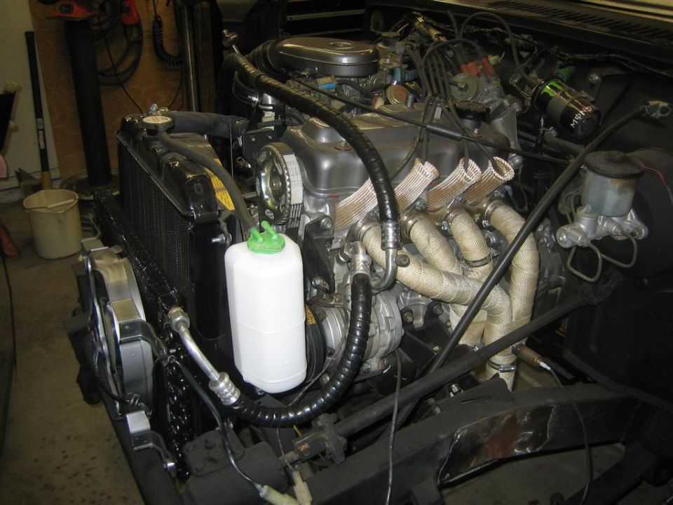 1987 Suzuki Samurai engine bay with exhaust manifold wrapped in heat tape, radiator, and coolant reservoir