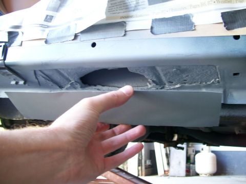 1995 Mercury Grand Marquis - Rust repair in progress on a lower rear body panel: a hand holds a piece of sheet metal patch against a rotted-through section where corrod…