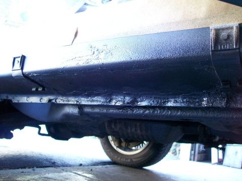 1995 Mercury Grand Marquis - Ground-level view of thick, freshly applied black rubberized undercoating along a rocker panel and lower body seam, with a wheel wearing a…