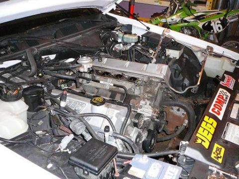 1997 Mercury Grand Marquis - Engine bay of a white car with the upper intake removed, exposing the engine valley; dirt bikes visible in the background.