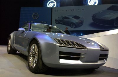 Silver concept sports car, front 3/4 view, on an auto show stand with Messenger display boards
