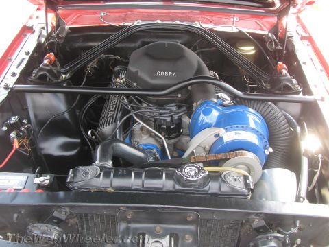 1968 Ford Mustang - Close-up view of a car's engine bay, highlighting a prominent blue supercharger and a black air intake cover labeled 'COBRA'.