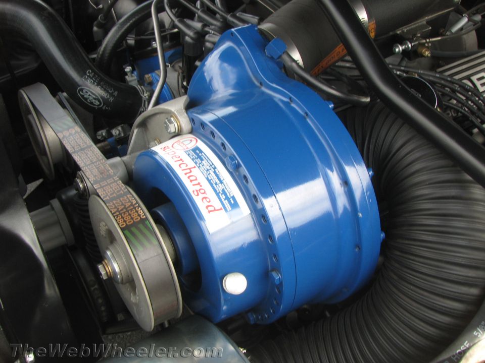 Engine bay with a blue supercharger and ribbed black hose