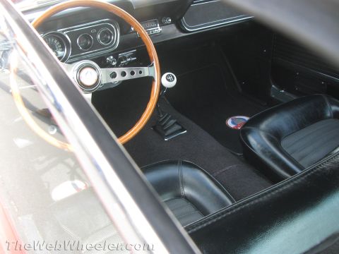1968 Ford Mustang - The interior of a 1968 Ford Mustang features a wooden steering wheel, a four-speed floor shifter, and black bucket seats.