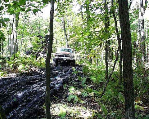 1988 Ford Bronco - Ford Bronco tackles a challenging muddy off-road course in a wooded area.