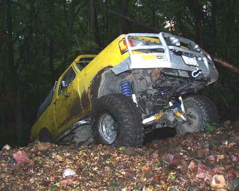 1988 Ford Bronco - A yellow off-road truck is stuck on a wooded, rocky trail.