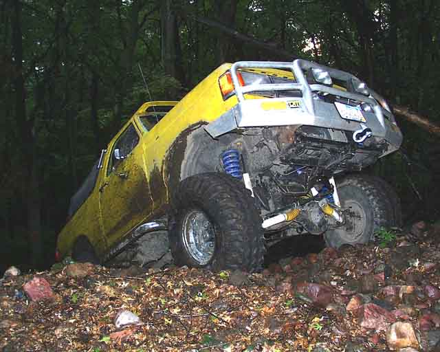 Yellow off-road truck with large tires and a silver bumper, stuck on a rocky incline