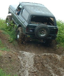 1988 Ford Bronco - 1988 Ford Bronco tackling a challenging muddy trail, showing its rear profile.