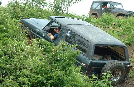 1988 Ford Bronco - Two off-road vehicles navigate a steep, overgrown trail.