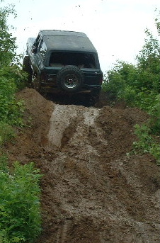 1988 Ford Bronco - A dark-colored SUV navigates a steep, muddy incline, kicking up dirt as it ascends.