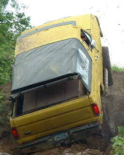 1988 Ford Bronco - This yellow SUV is navigating a steep, muddy incline, with its soft top in the raised position.