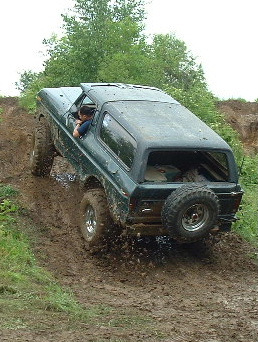 1988 Ford Bronco - A Ford Bronco navigates a challenging muddy incline, demonstrating its off-road capabilities.