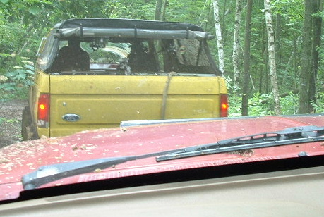1988 Ford Bronco - Two vehicles navigate a wooded area, with one yellow SUV partially visible from behind.