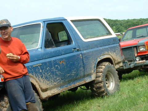 1988 Ford Bronco - Two off-road vehicles, a blue Ford Bronco and a red Jeep Cherokee, are parked in a grassy field.