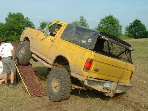 1988 Ford Bronco - A muddy yellow SUV navigates a ramp, its tires kicking up dirt.