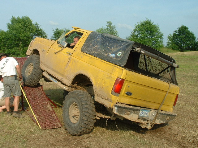 Yellow soft-top Ford Bronco climbing a steel ramp obstacle at a 4x4 event
