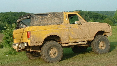 1988 Ford Bronco - This yellow 1988 Ford Bronco, heavily coated in mud, is viewed from the front-three-quarter angle, suggesting off-road use.