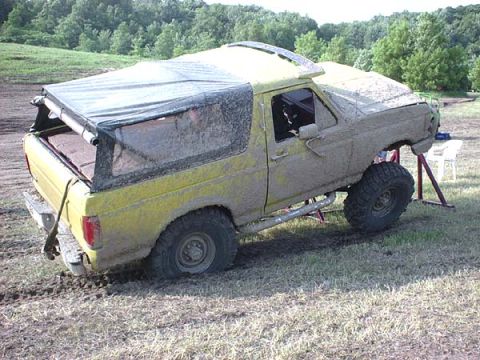 1988 Ford Bronco - This heavily modified SUV, likely from the 1980s, is covered in mud and appears to be stuck in a muddy field.