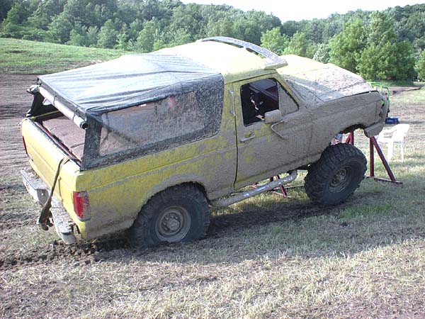 Mud-covered yellow SUV with a soft top, lifted suspension, and off-road tires, stuck in mud