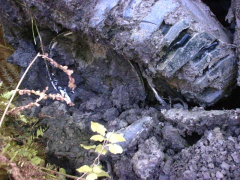 1988 Ford Bronco - A close-up view of a tire stuck in the mud, partially obscured by dirt and plants.