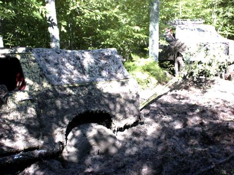 1988 Ford Bronco - Two off-road vehicles are deeply stuck in mud and dirt, surrounded by trees and foliage.