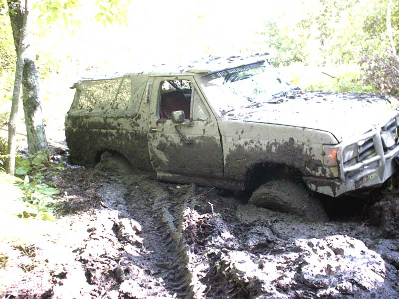 1988 Ford Bronco stuck deep in mud off-road, front right wheel submerged