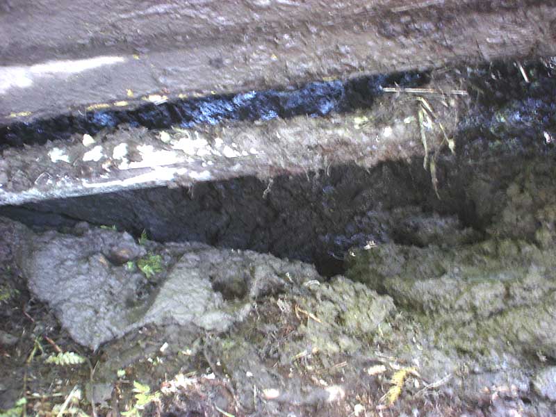 Mud-caked rocker panel and frame rail of a vehicle high-centered over a muddy trench
