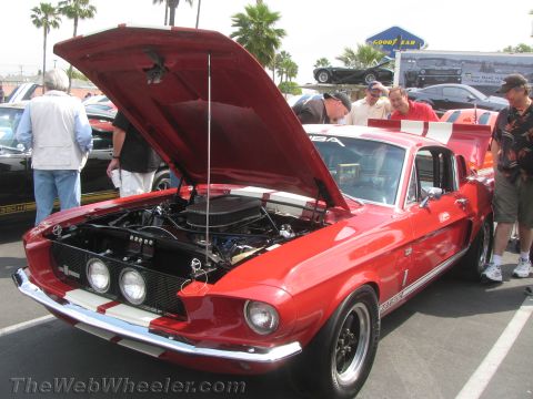 1968 Ford Mustang - A red 1968 Ford Mustang Shelby GT500 is displayed with its hood open, revealing the engine bay to onlookers.