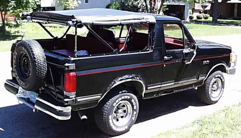 Black Ford Bronco, top removed, red interior, rear 3/4 view in driveway