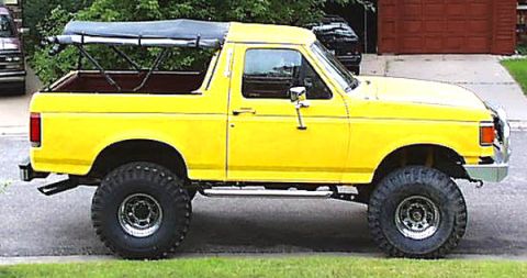 1988 Ford Bronco - A yellow Ford Bronco with a soft top is parked on the side of the road.