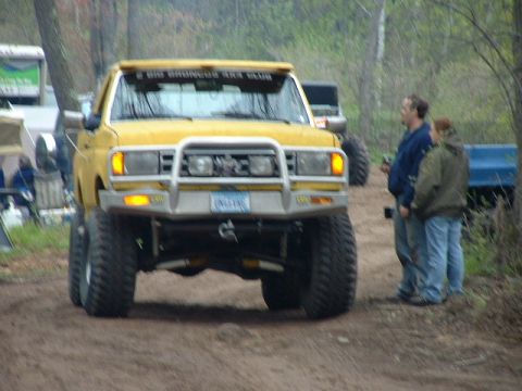 1988 Ford Bronco - A yellow lifted truck with a custom bumper and off-road tires is parked on a dirt path.